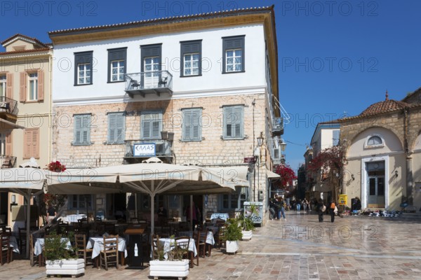 A square with a historic building, café with parasols and Mediterranean flair under a blue sky,