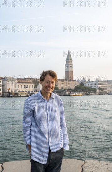 Young man in striped shirt and shorts on the banks of the Grand Canal, looking into the camera,
