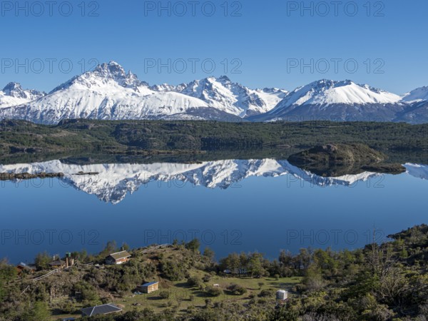The snow-covered Mt. Cerro Castillo is reflected in a lake, small farm by the lake, Patagonia,