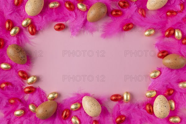 Frame made of eggs on pink feathers with red and gold chocolate eggs on a pink background