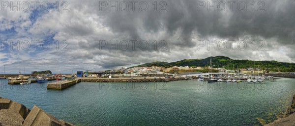 Coastal harbour with boats and houses surrounded by mountains under a cloudy sky, small town of
