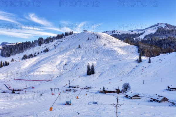 Snowy winter landscape with ski lift and huts against a clear blue sky, Sudelfeld