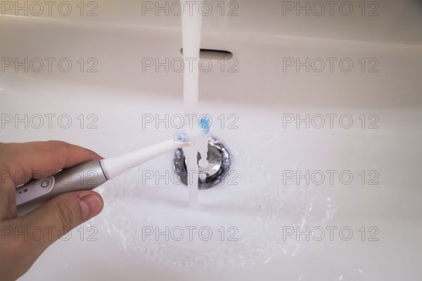 A bathroom tap is running while a toothbrush is held under the running water, symbolic image of