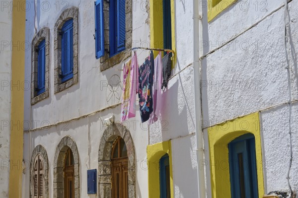 Colourful laundry hanging between houses with blue and yellow shutters and white walls, Platia,