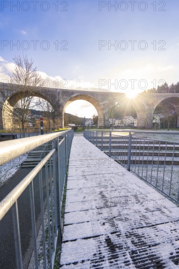 Wooden walkway with snow under a viaduct at dusk, with clear sky and bright light, forest ball from