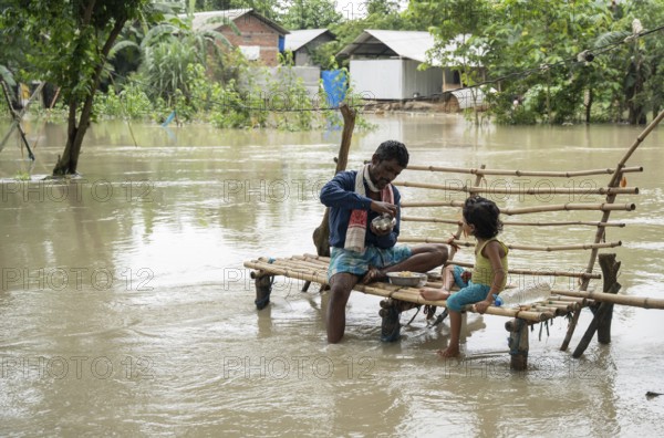 Morigaon, India. 4 July 2024. Father with his daughter eating food, in a flood affected village in
