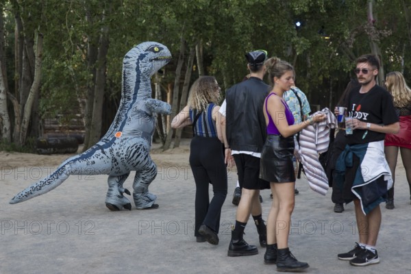 A festival visitor dressed as a dinosaur walks through the forest alongside other guests at the