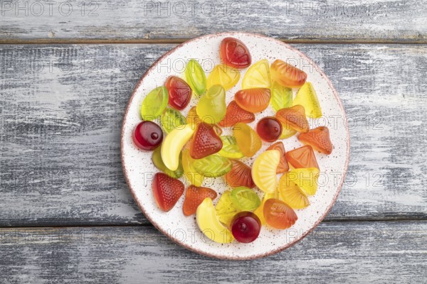 Various fruit jelly candies on plate on gray wooden background. top view, flat lay, close up