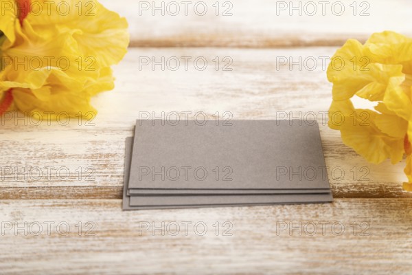 Gray business card with iris yellow flowers on white wooden background. side view, copy space,