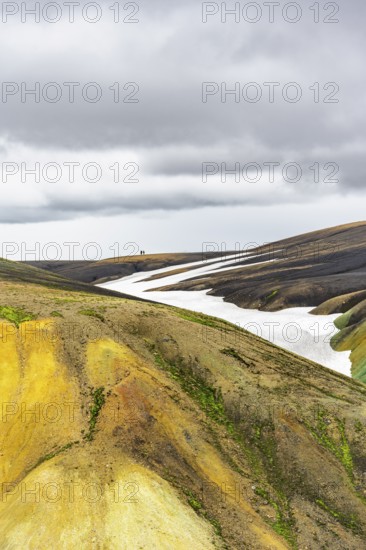 Two hikers on a hill in the distance, colourful volcanic landscape with hills and snow, Laugavegur