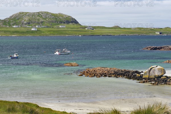 Some boats on the sea in front of a rocky coast, island with houses, view of Iona, Port of