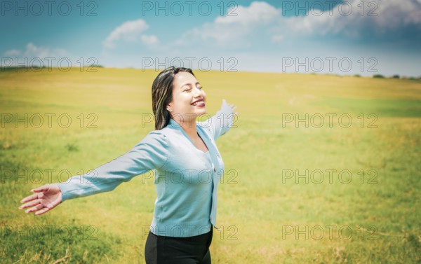Serene young woman breathing fresh air in beautiful field spreading arms. Happy girl spreading arms