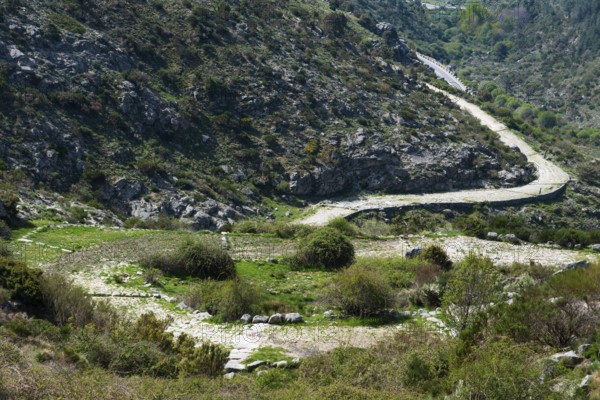 A winding path runs through a hilly and green landscape with rocky elevations, old Roman road, at