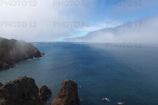 Steep cliffs jut into the blue sea under a cloudy sky, fog, Cape Cabo da Roca, westernmost point of