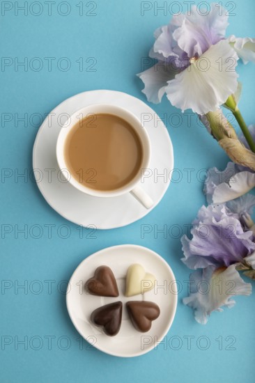 Cup of cioffee with chocolate candies and lilac iris flowers on blue pastel background. top view,