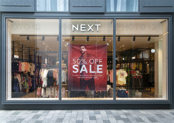 Poster advertising 50% off sale in shop window of Next sture, Newbury, Berkshire, England, UK