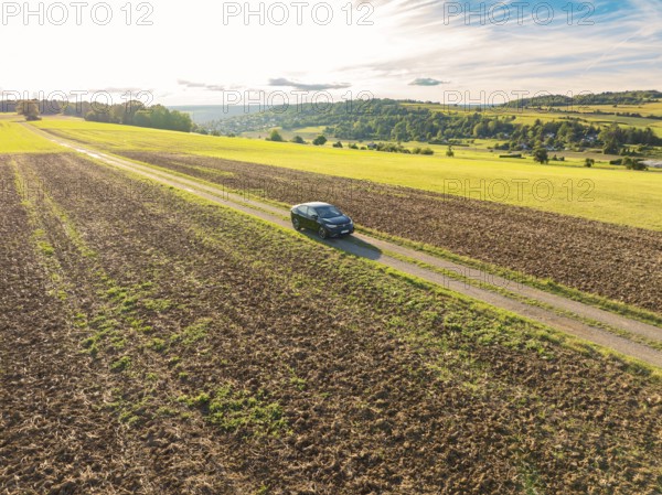 Black car on a rural country lane between fields in a vast rural landscape, car sharing, VW ID5,