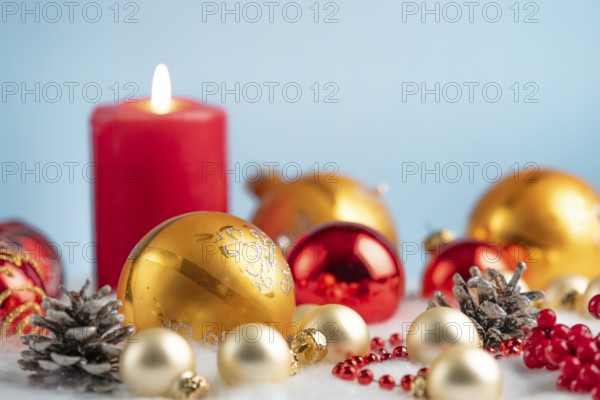 Burning candle with red and gold baubles and pine cones on artificial snow, festive atmosphere