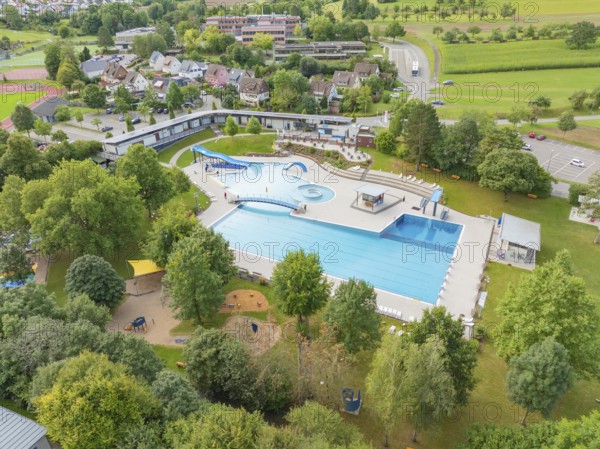 Aerial view of an outdoor swimming pool with several pools, slides and surrounding trees in a green