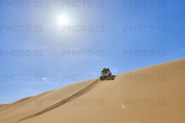 Off-road vehicle drives over a sand dune under a bright blue sky in the desert, Matruh, Great Sand