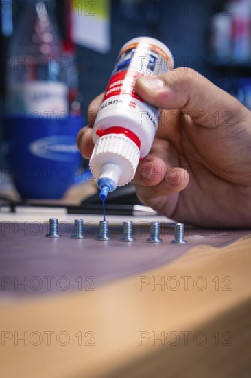 Hand applying blue liquid to screws on a workbench, Waldbike Manufaktur, bicycle workshop, Calw,