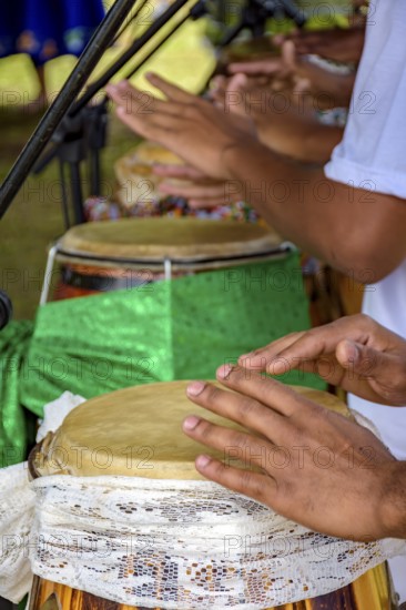 Hands playing several atabaque drums decorated with fabric being used during an Umbanda religious
