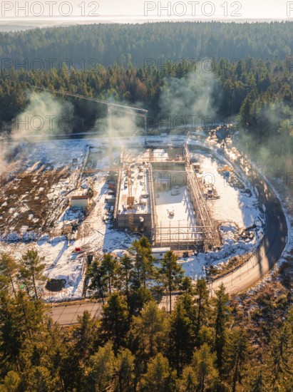 Snow-covered construction site in the forest with cranes and areas surrounding trees, new fire