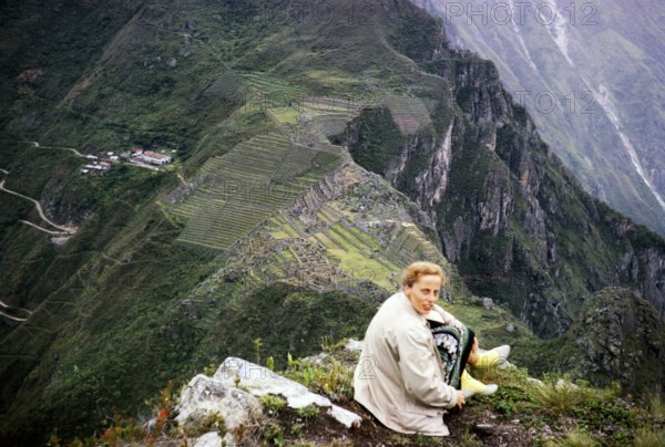 Female tourist sitting on the mountain Huayna Picchu with view of Machu Picchu, Peru, South America
