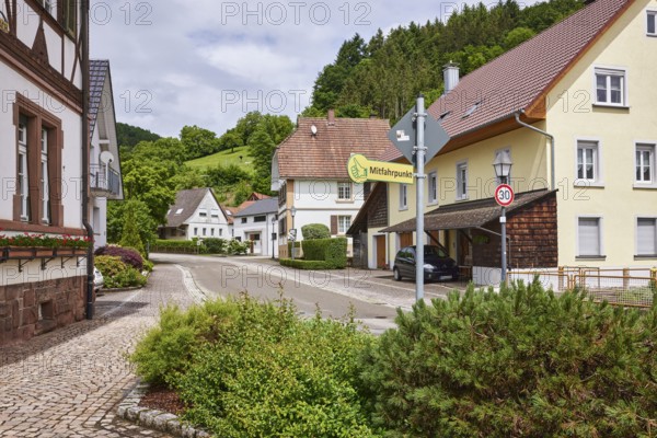 Carpooling point, multi-family houses, hilly landscape with coniferous forest, overcast sky with
