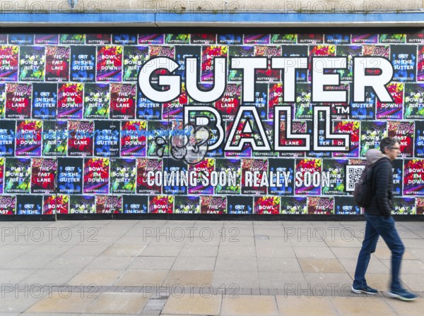 Person waking past posters on shopfront advertising Gutter Ball ten pin bowling attraction,