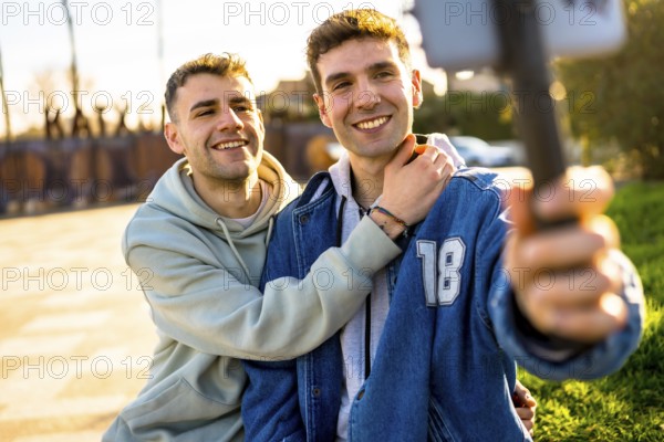 Two men in love are hugging and taking a selfie with a smartphone, enjoying a sunny day outdoors