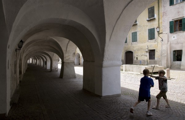 Italy S-Tyrol Neumarkt Laubengasse with view to the alleyway fountain and playing boys