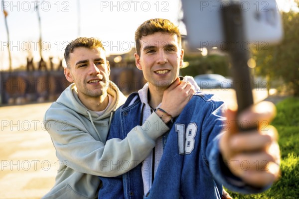 Two men in love embracing each other while capturing a joyful selfie with a smartphone mounted on a