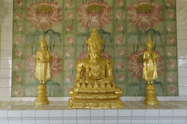 Three golden statues on a pedestal in front of ornately decorated walls inside the temple, penang,