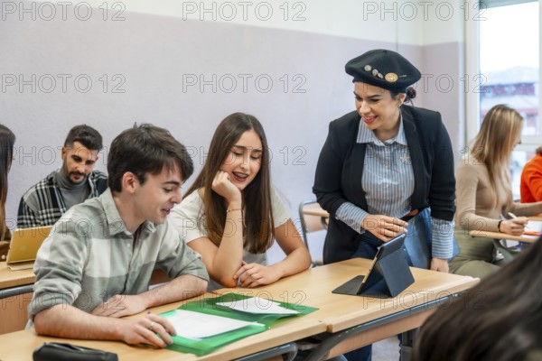University teacher using tablet explaining lesson to two students sitting at desk in classroom