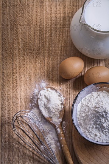 Aerial view copyspace composition pitcher with milk flour in bowl and spoon eggs corolla on wooden