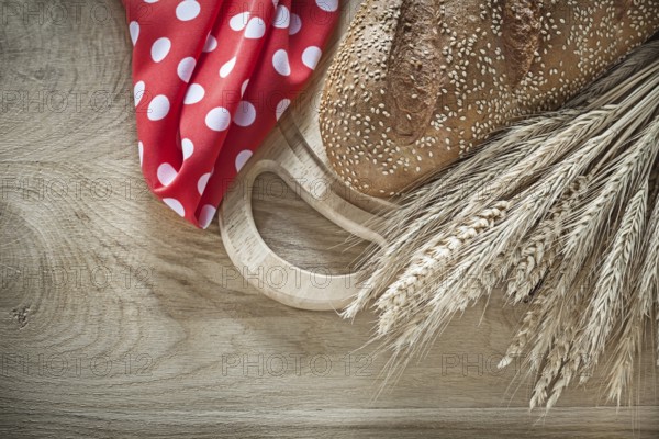 Bread chopping board wheat ears red tablecloth on wooden background