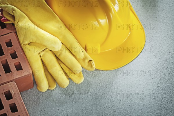 Assortment of red bricks hard hat safety gloves on concrete background construction concept