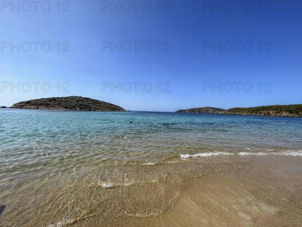 Calm beach with gentle waves and hills in the background under a blue sky, cagliari, sardinia,