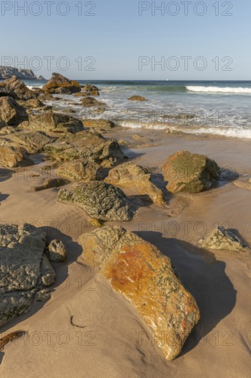 A rocky beach with a large rock in the foreground and a boat in the distance. The beach is quiet