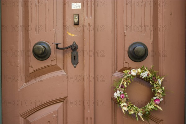 Detail of an antiquated front door with floral wreath and no advertising sign in a building on the
