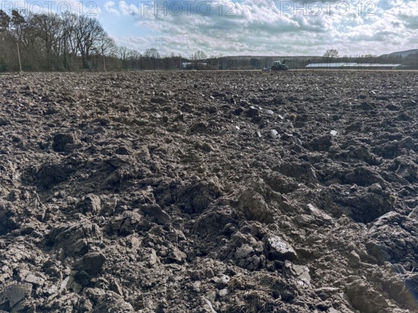 Freshly ploughed field in spring, tractor with plough in the background, Germany, Europe