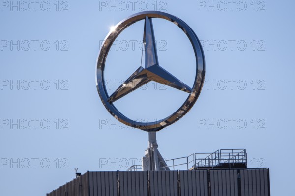 Large Mercedes-Benz logo on the roof of a modern building under a clear blue sky, star,