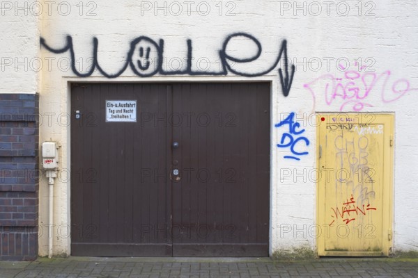 View of a graffiti-painted house facade with garage door and small entrance door, vandalism, street