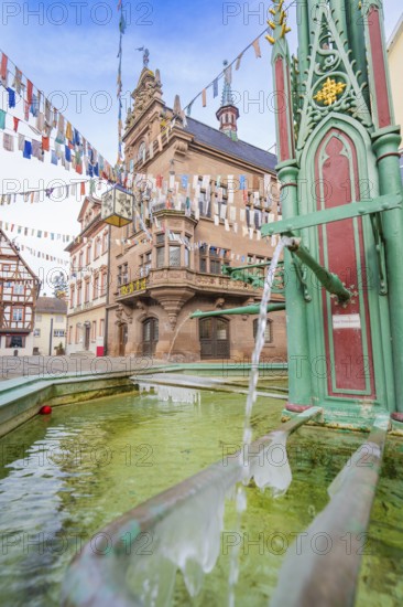 Historic town centre with green fountain and colourful pennants in front of an old building,