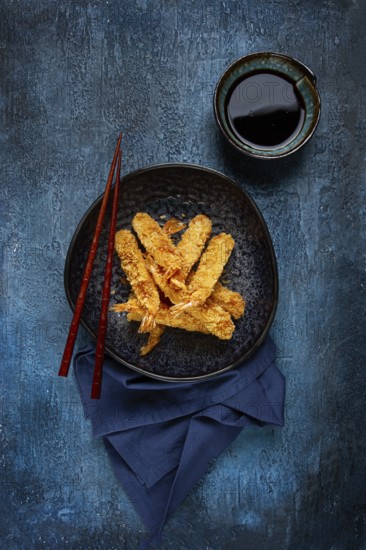 Shrimp in tempura, deep fried, on a black plate, with soy sauce, close-up, top view, no people