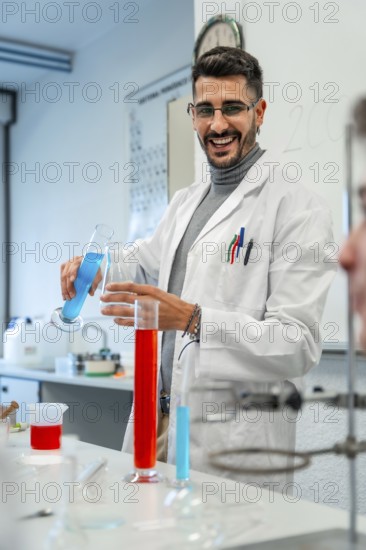 Young male scientist pouring blue liquid into laboratory glassware while smiling during an