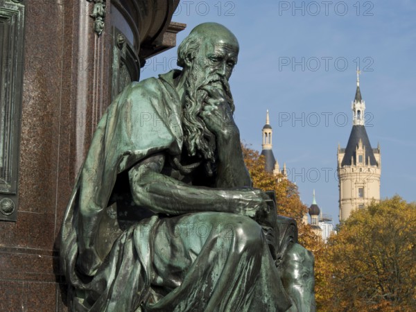 Bronze statue of a pensive man in front of a historic castle on an autumn day, Schwerin, Germany,