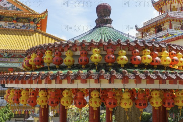 Richly decorated pavilion with hanging red and yellow lanterns. Temple in the background, penang,
