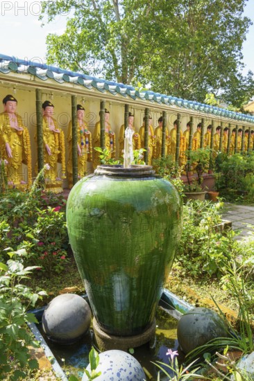Garden with large ceramic pot, plants and Buddha figures along a wall, penang, malaysia